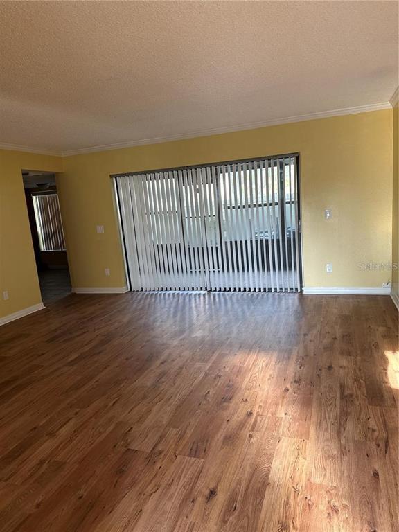 An empty living room with yellow walls, wood-look flooring, and vertical blinds over sliding doors — 4725 PURITAN CIRCLE UNIT 603, TAMPA, FL