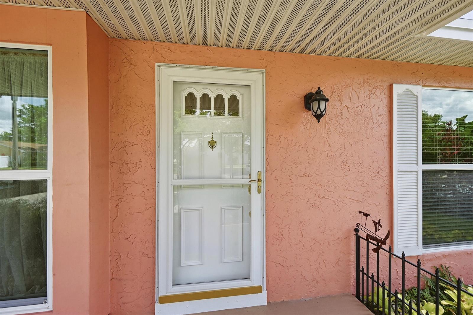 A peach-colored exterior wall features a white storm door, a wall lamp, and two windows — 8131 Countrypark Drive, Boca Raton FL 33433, BOCA RATON, FL