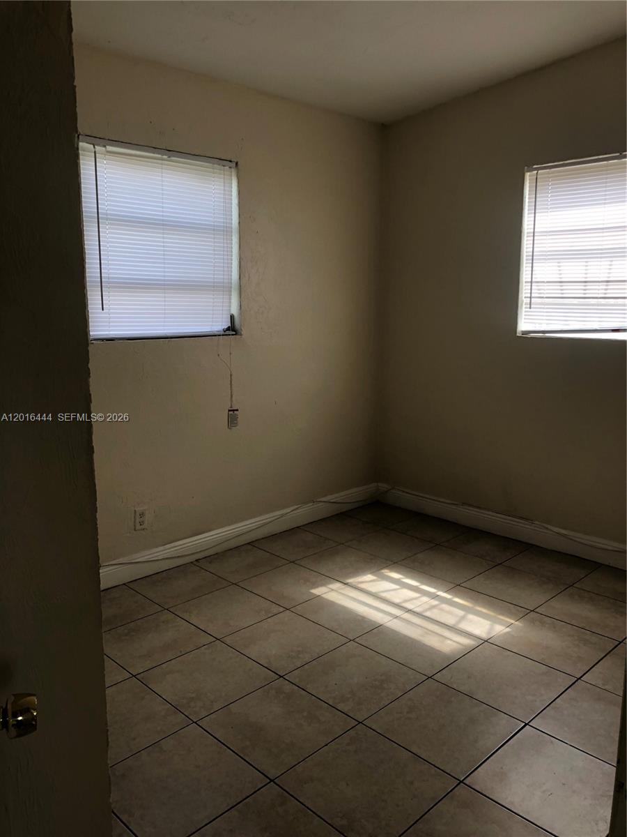 An empty room features beige walls, tiled flooring, and two windows with white blinds — 640 SW 7th St, Homestead FL 33030, HOMESTEAD, FL