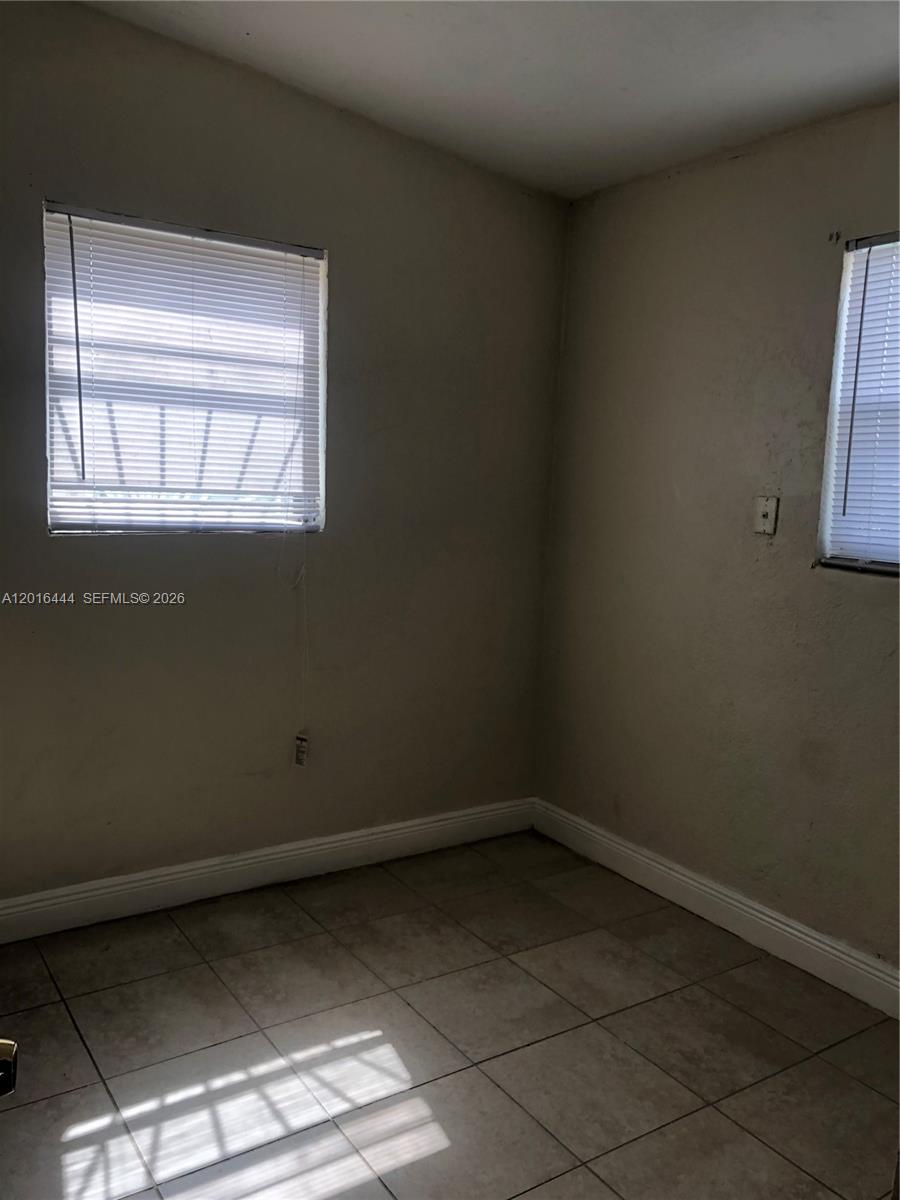 An empty room features beige walls, tiled flooring, and two windows with white blinds — 640 SW 7th St, Homestead FL 33030, HOMESTEAD, FL