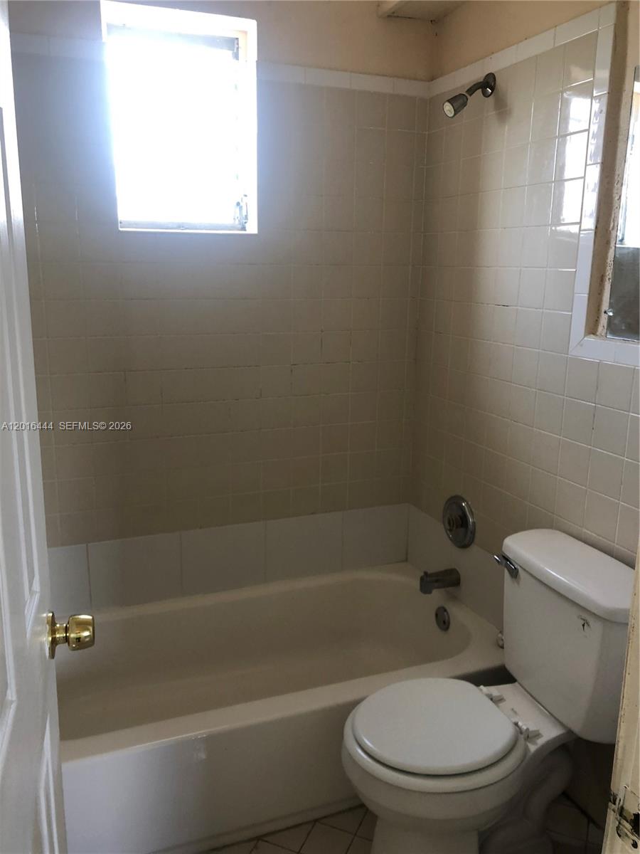 A bathroom features a white bathtub, a toilet, and beige tiled walls around the shower — 640 SW 7th St, Homestead FL 33030, HOMESTEAD, FL