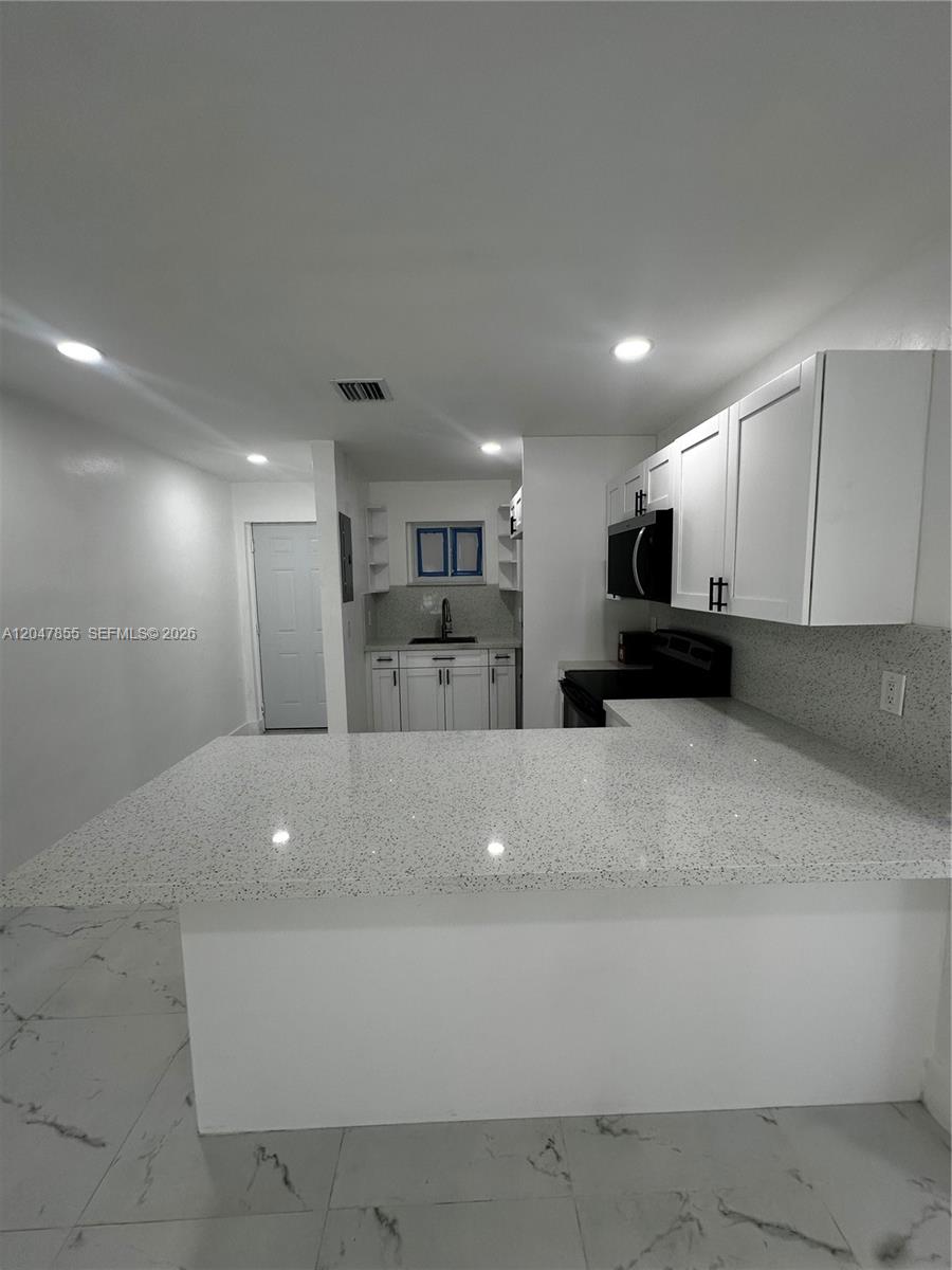 A kitchen features white cabinets, speckled countertops, and a breakfast bar overlooking a tiled floor — 1945 NW 29th St # A5, Miami FL 33142, MIAMI, FL