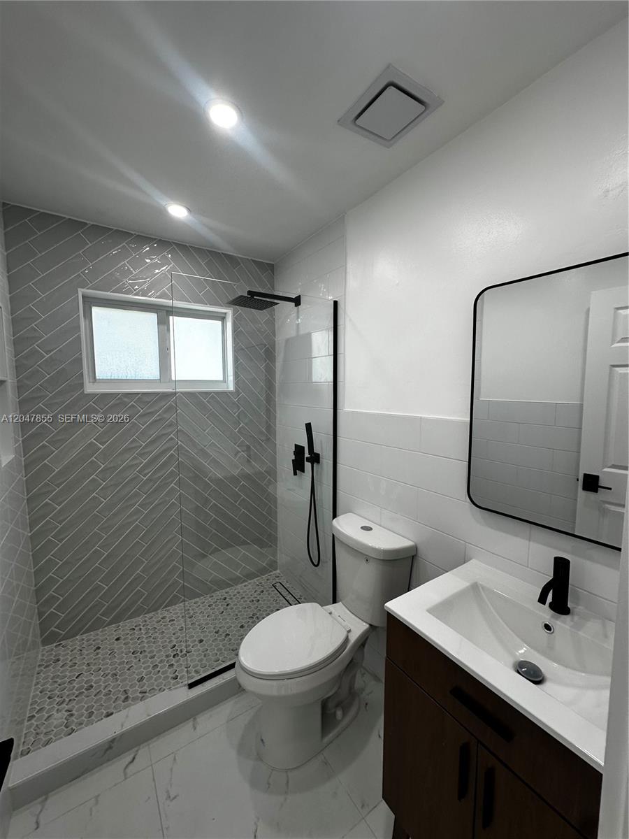 A modern bathroom features a glass-enclosed shower with gray herringbone tile and pebble flooring — 1945 NW 29th St # A5, Miami FL 33142, MIAMI, FL