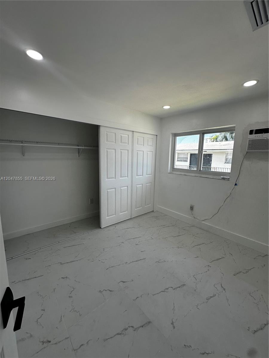 A bedroom features white marble-look tile flooring, recessed lighting, a sliding closet, and a window — 1945 NW 29th St # A5, Miami FL 33142, MIAMI, FL