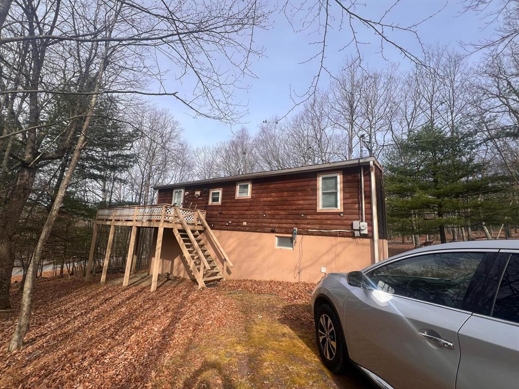 A wooden house with a raised deck and stairs sits on a sloped, wooded lot — 123 ROCKY ROAD, LACKAWAXEN, PA