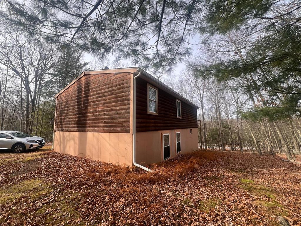 A two-story house with log-style siding and a tan foundation sits in a wooded area — 123 ROCKY ROAD, LACKAWAXEN, PA