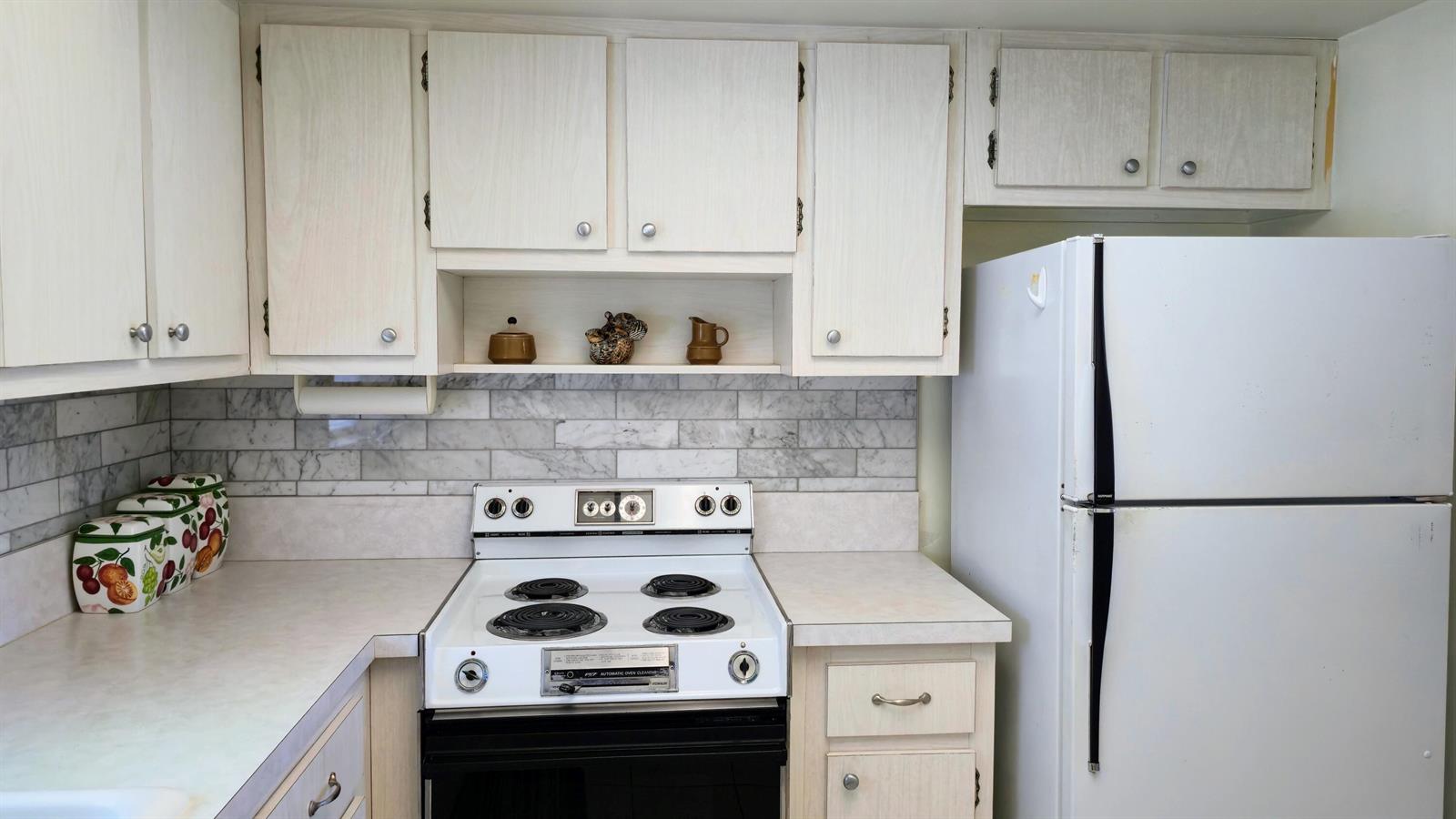 A kitchen features white cabinets, a white electric stove, and a marble-style subway tile backsplash — 2800 Ashley Drive E # B, West Palm Beach FL 33415, WEST PALM BEACH, FL