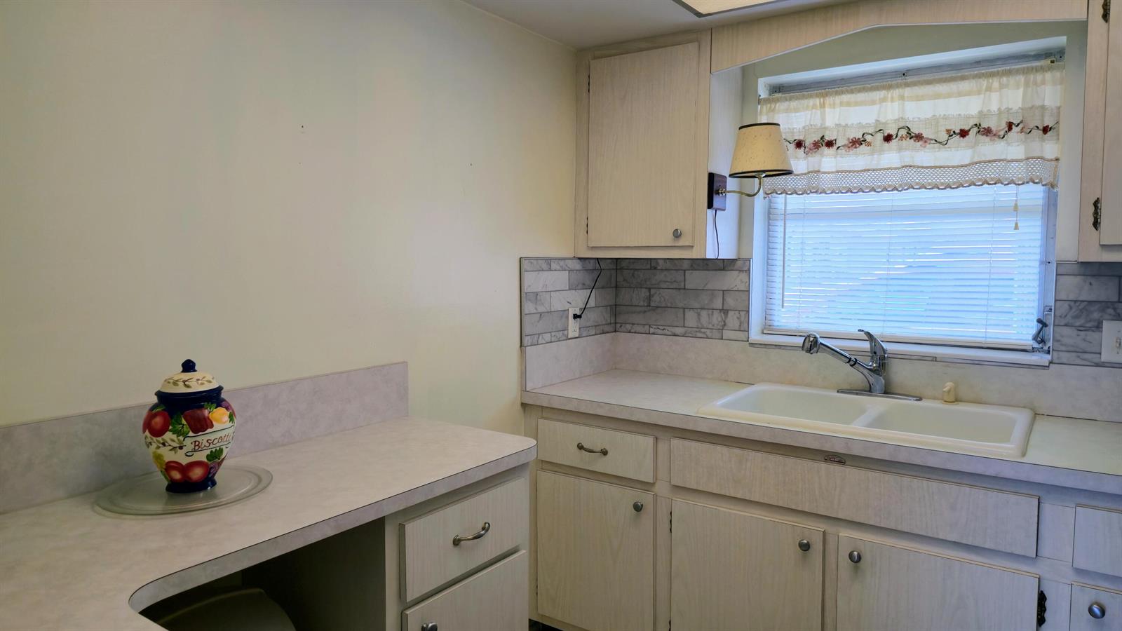 A kitchen features light wood cabinets, a white double sink, and a marble-look tile backsplash — 2800 Ashley Drive E # B, West Palm Beach FL 33415, WEST PALM BEACH, FL