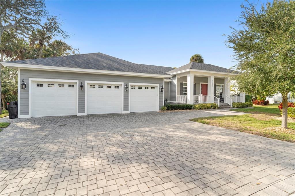 A gray house with a three-car garage and a front porch sits behind a paver driveway — 1702 SAXON DRIVE, NEW SMYRNA BEACH, FL