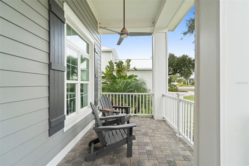 A covered porch features gray siding, two dark Adirondack chairs, and a ceiling fan — 1702 SAXON DRIVE, NEW SMYRNA BEACH, FL