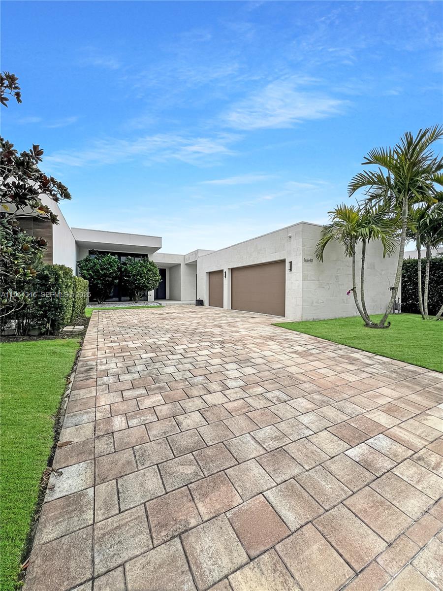 A paved driveway leads to a modern house with a multi-car garage and palm trees — 16640 Sunset Way, Weston FL 33326, WESTON, FL
