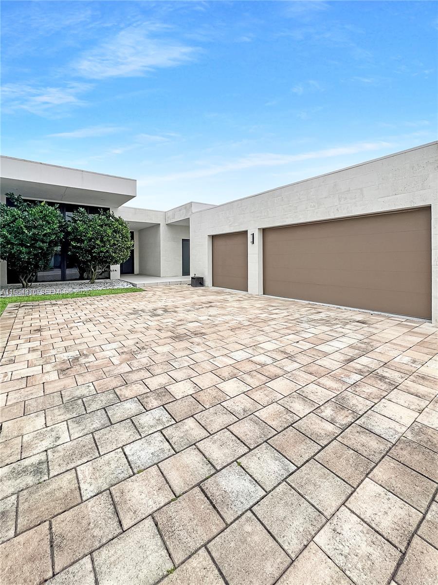 A modern house exterior features a paved driveway, two garage doors, and two small trees — 16640 Sunset Way, Weston FL 33326, WESTON, FL