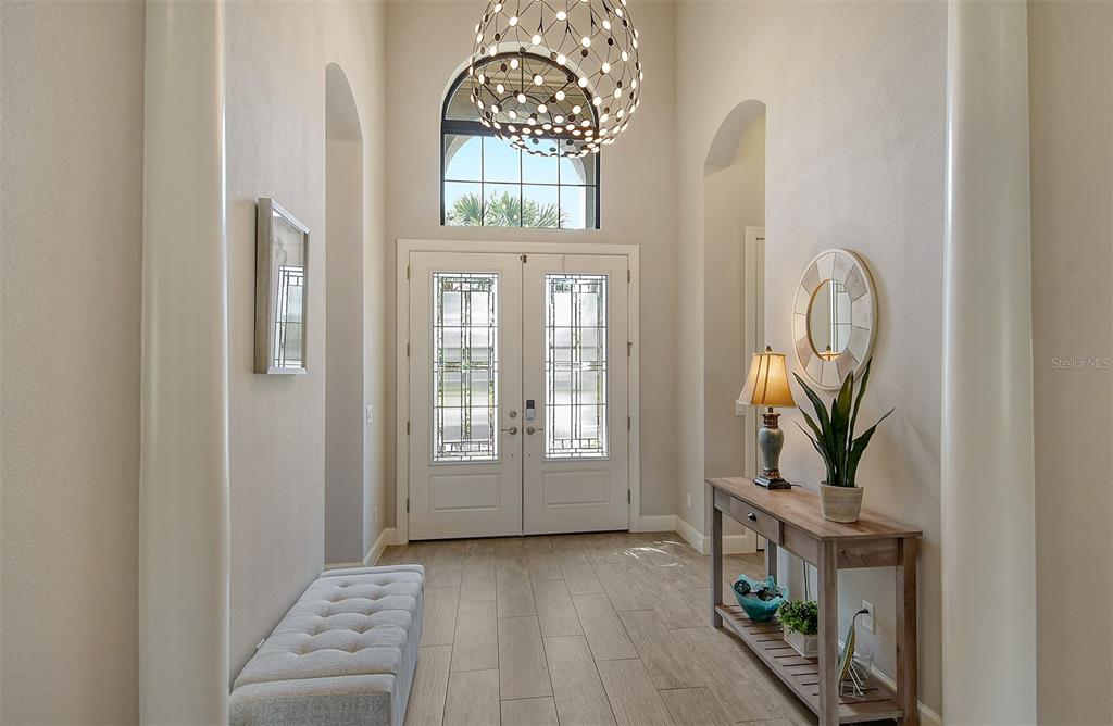 A bright entryway features a double front door, a modern chandelier, and wood-look tile flooring — 4735 CABREO COURT, LAKEWOOD RANCH, FL