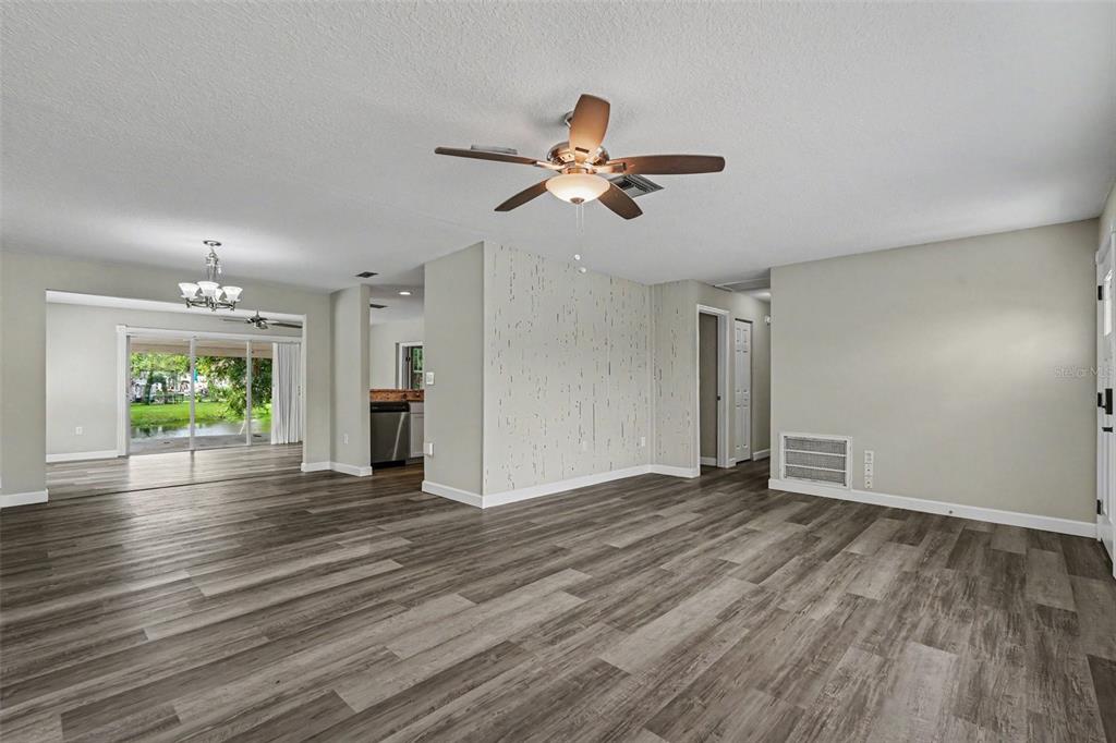 A living room with wood-look flooring, a ceiling fan, and a textured accent wall — 6822 LASSEN AVENUE, NEW PORT RICHEY, FL