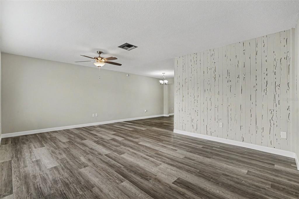 An empty living room features wood-look flooring, a ceiling fan, and a distressed wood-paneled wall — 6822 LASSEN AVENUE, NEW PORT RICHEY, FL