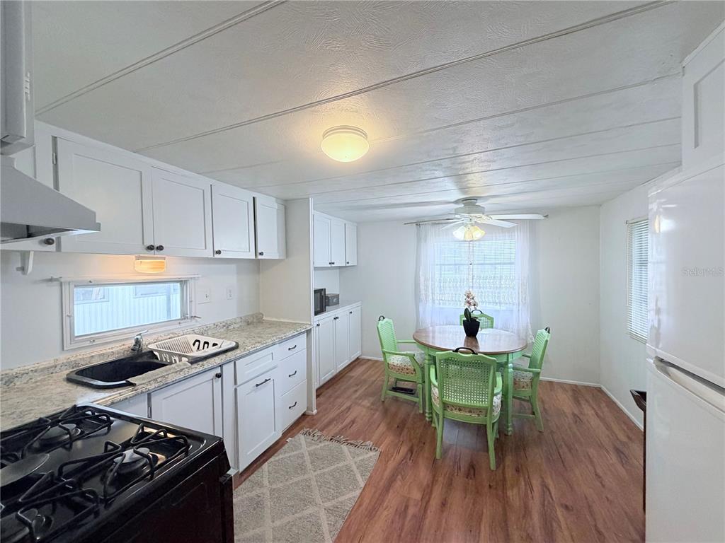 A kitchen with white cabinets, a black sink, and a dining area with green chairs — 1800 ENGLEWOOD UNIT 36, ENGLEWOOD, FL