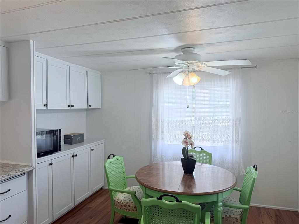 A dining area features a round wooden table, green chairs, white cabinetry, and a ceiling fan — 1800 ENGLEWOOD UNIT 36, ENGLEWOOD, FL