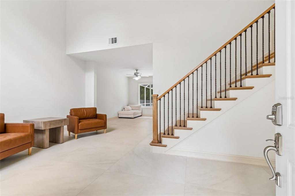 A bright entryway features white tile floors, a wooden staircase with iron railings, and leather chairs — 4966 EBENSBURG DRIVE, TAMPA, FL