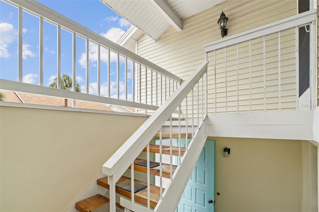 An exterior view of a wooden staircase leading to an upper balcony with white railings — 12239 SUN VISTA COURT E, TREASURE ISLAND, FL