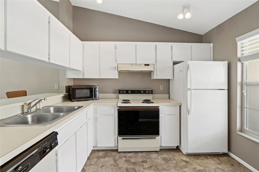 A kitchen with white cabinets, white appliances, a double sink, and brown tile flooring — 12239 SUN VISTA COURT E, TREASURE ISLAND, FL