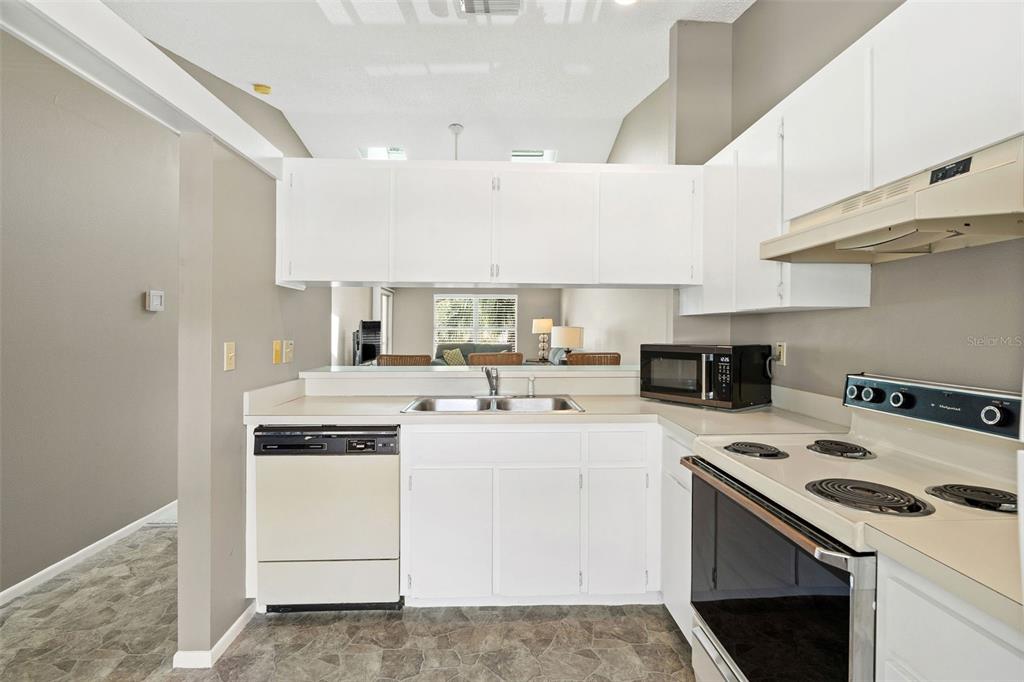 A kitchen with white cabinets, a double sink, a dishwasher, and a black electric stove — 12239 SUN VISTA COURT E, TREASURE ISLAND, FL