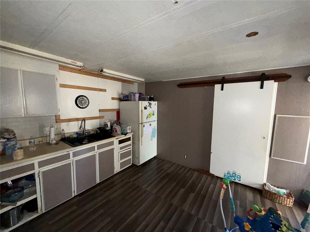 A kitchen features dark wood-look flooring, white cabinets, a refrigerator, and a sliding barn door — 10904 ROSS ST, TAMPA, FL