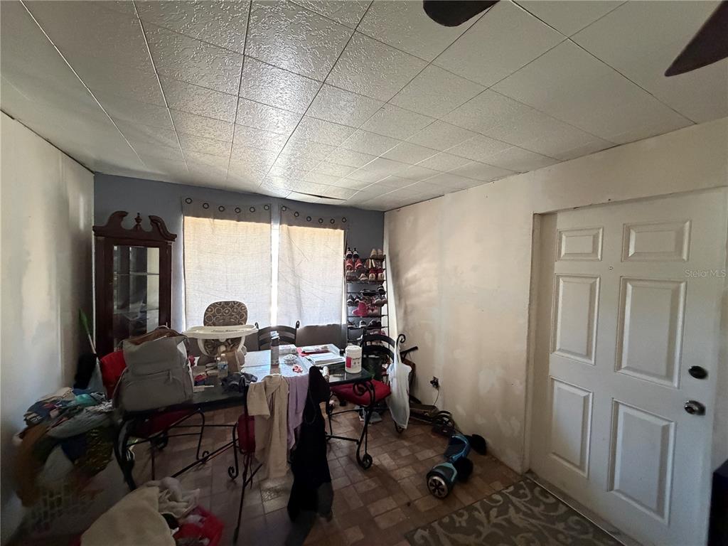 A cluttered dining area features a tile floor, a drop ceiling, and a white door — 10904 ROSS ST, TAMPA, FL