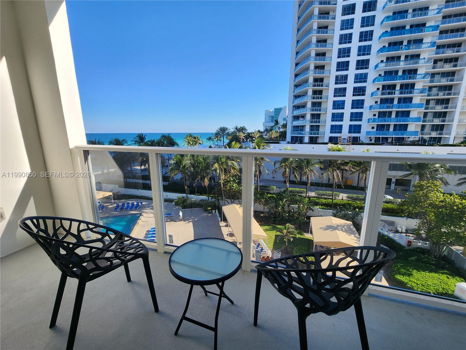 A balcony features two black chairs, a small glass table, and a view of the ocean — 3505 S Ocean Dr # 515, Hollywood FL 33019, HOLLYWOOD, FL