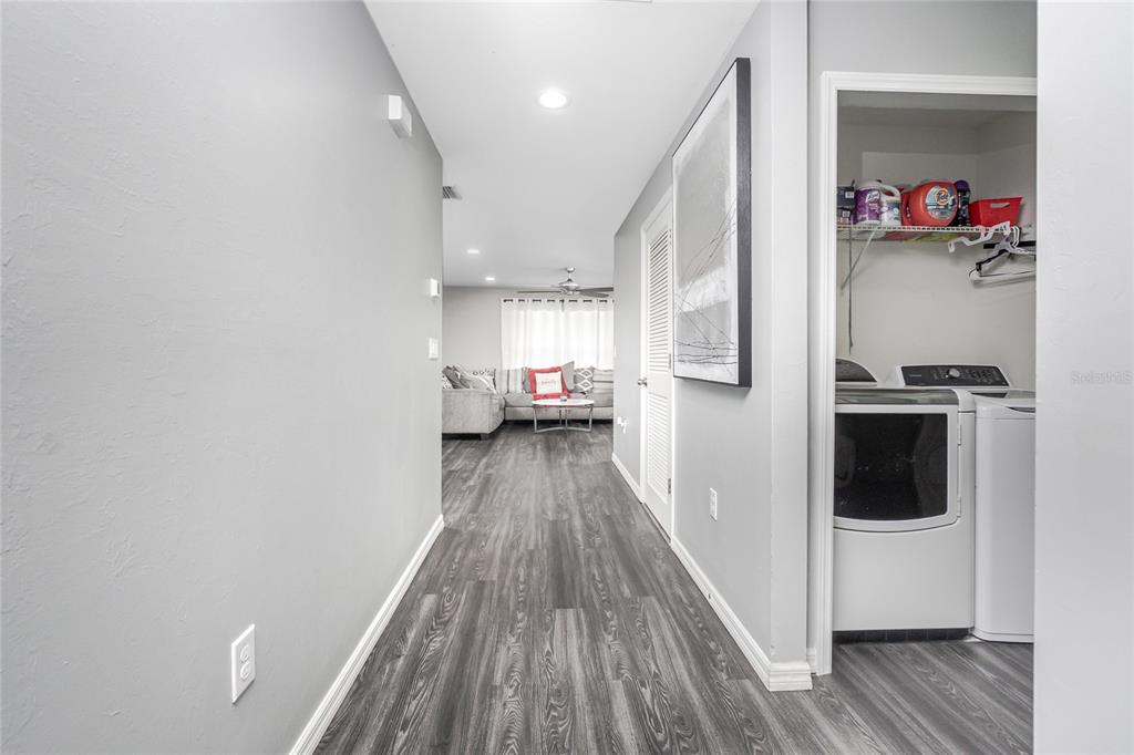 A hallway with gray wood-look flooring leads to a living room, with a laundry closet adjacent — 1203 DESMOND STREET, PORT CHARLOTTE, FL
