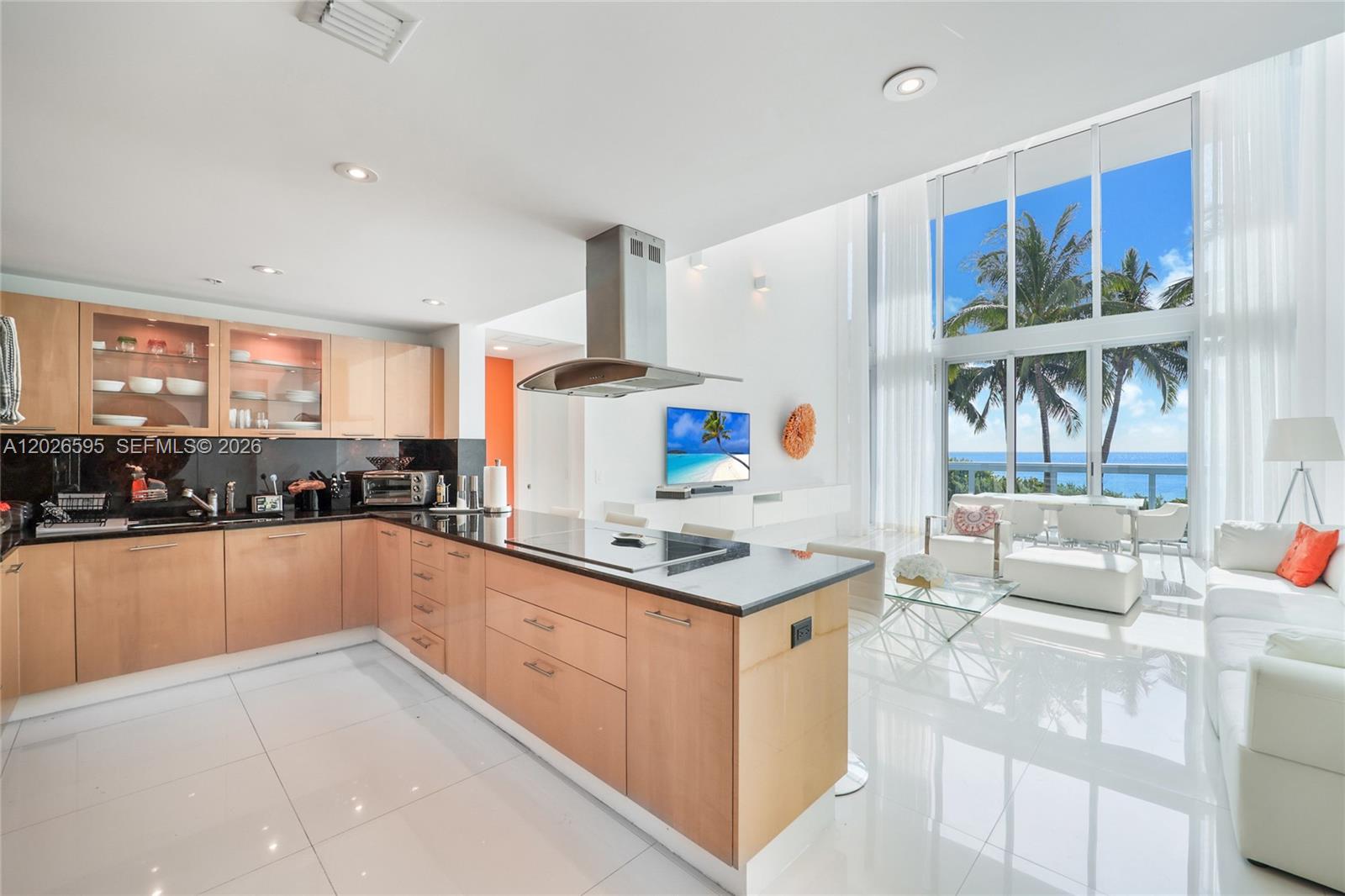 A modern kitchen and living area feature light wood cabinets, black countertops, and floor-to-ceiling windows — 6899 Collins Ave # 204, Miami Beach FL 33141, MIAMI BEACH, FL