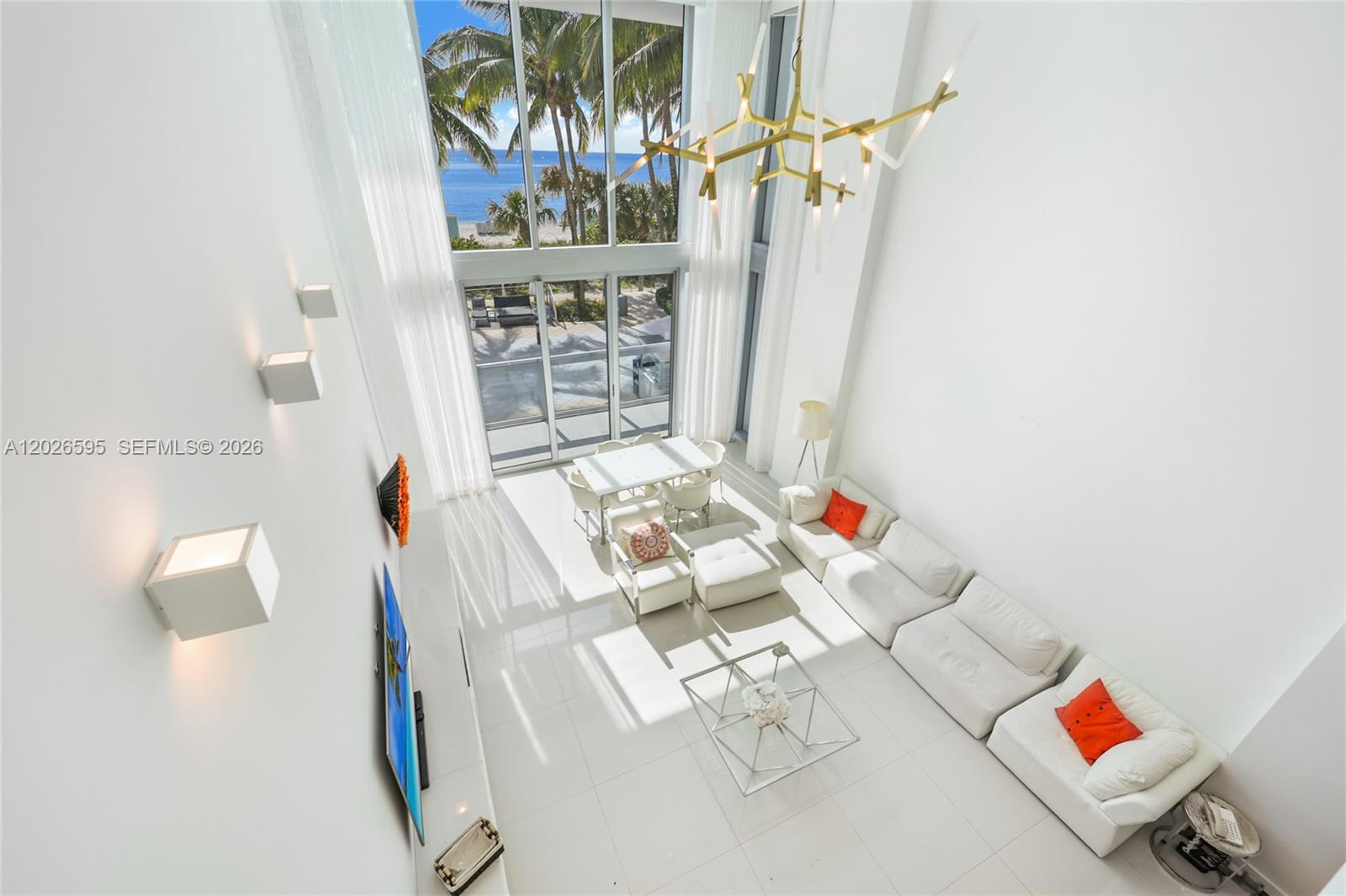 A high-ceilinged living room features white furniture, a glass coffee table, and floor-to-ceiling windows — 6899 Collins Ave # 204, Miami Beach FL 33141, MIAMI BEACH, FL