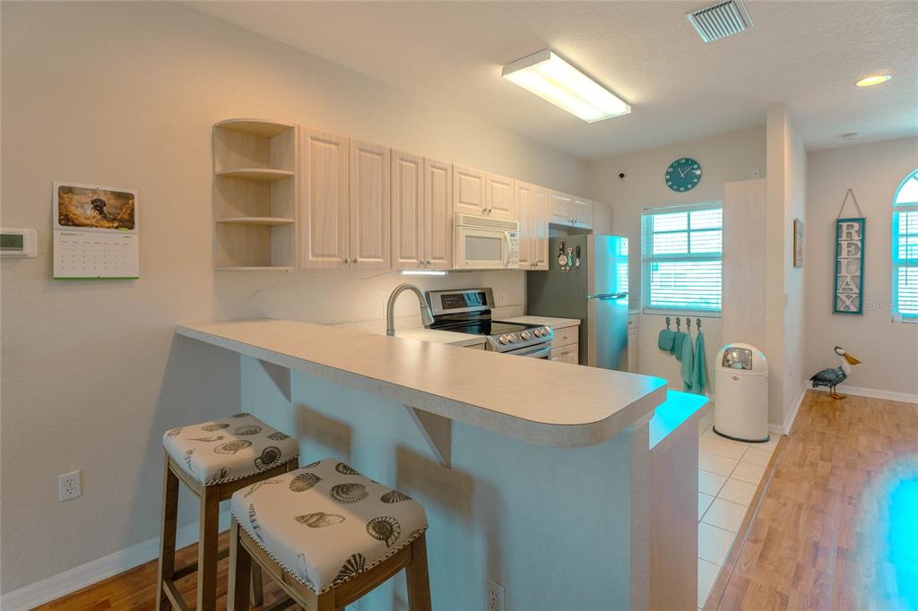 A kitchen features light wood cabinets, a breakfast bar with two stools, and stainless appliances — 3919 CAPE HAZE DRIVE UNIT 503, ROTONDA WEST, FL