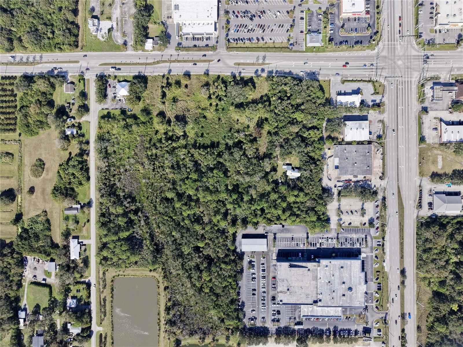 This aerial view shows a large, wooded lot surrounded by commercial buildings and roads — 511 W Midway Road, Fort Pierce FL 34982, FORT PIERCE, FL