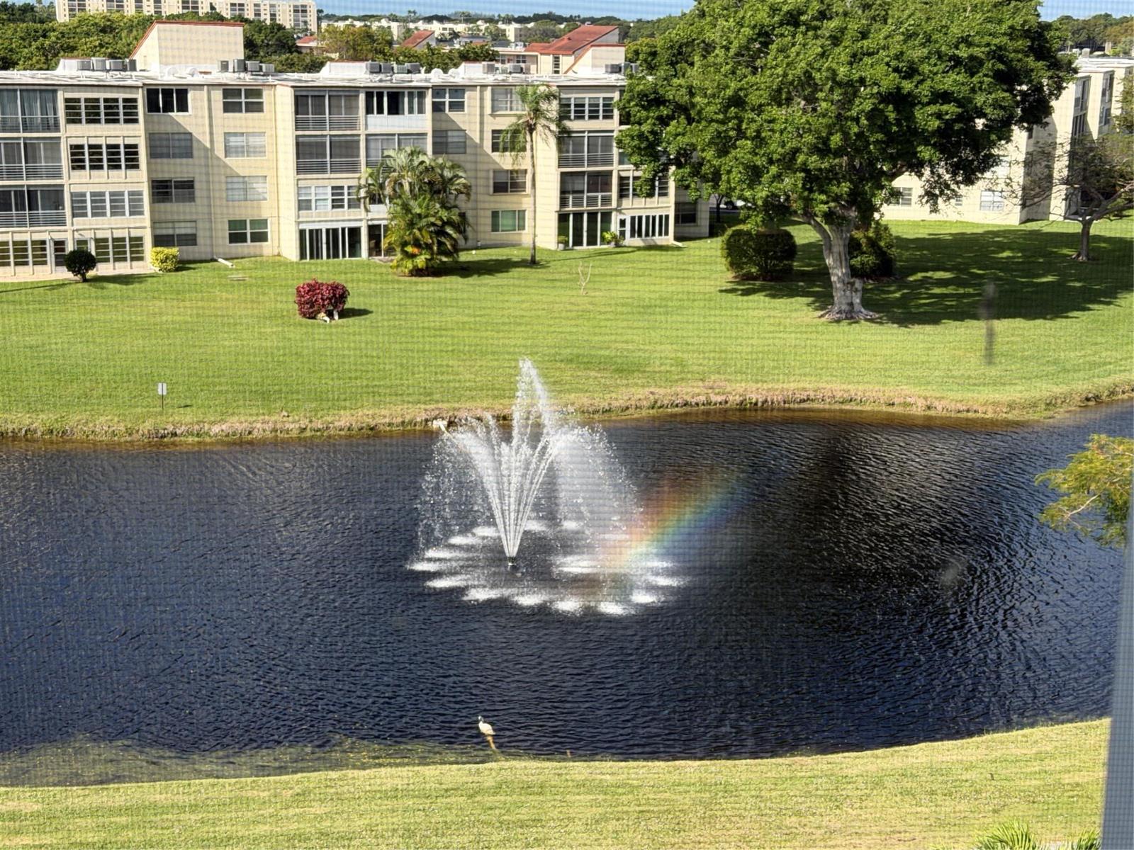 A view of a pond with a fountain and rainbow in front of apartment buildings — 14671 Bonaire Boulevard # 604, Delray Beach FL 33446, DELRAY BEACH, FL