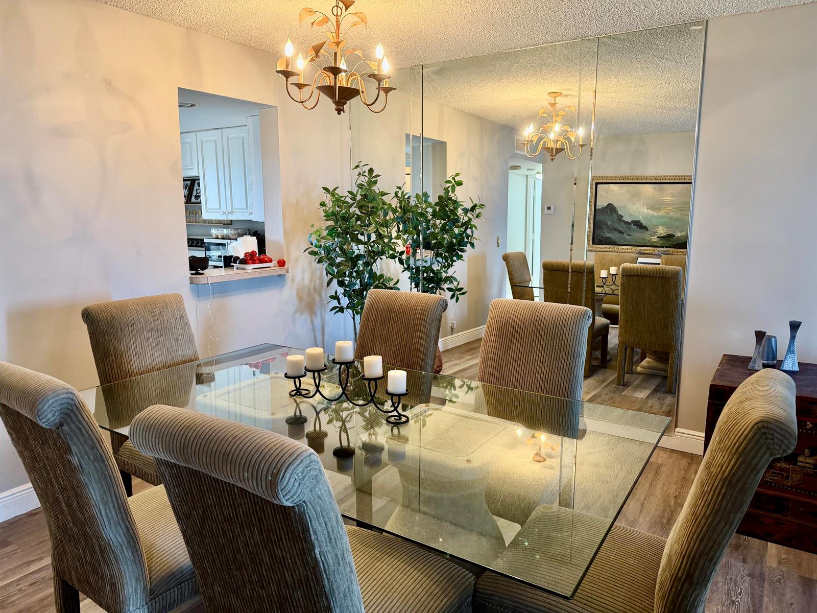 A dining room features a glass-topped table, upholstered chairs, a chandelier, and a mirrored wall — 14671 Bonaire Boulevard # 604, Delray Beach FL 33446, DELRAY BEACH, FL