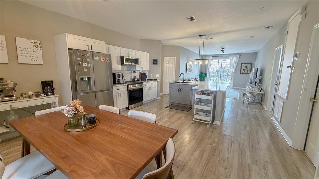 An open-concept kitchen and dining area features white cabinetry, stainless steel appliances, and wood-look flooring — 310 SUNSET VIEW DRIVE, DAVENPORT, FL