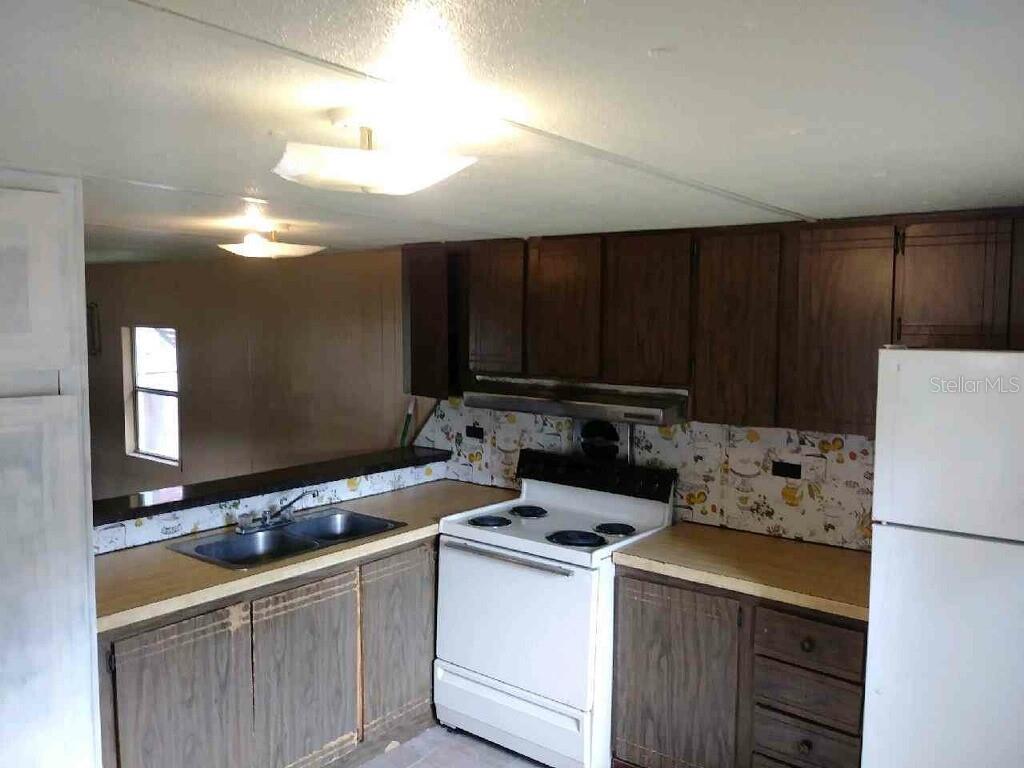 A kitchen features dark wood cabinets, a white stove, a white refrigerator, and floral wallpaper — 805 PETERS STREET, WILDWOOD, FL