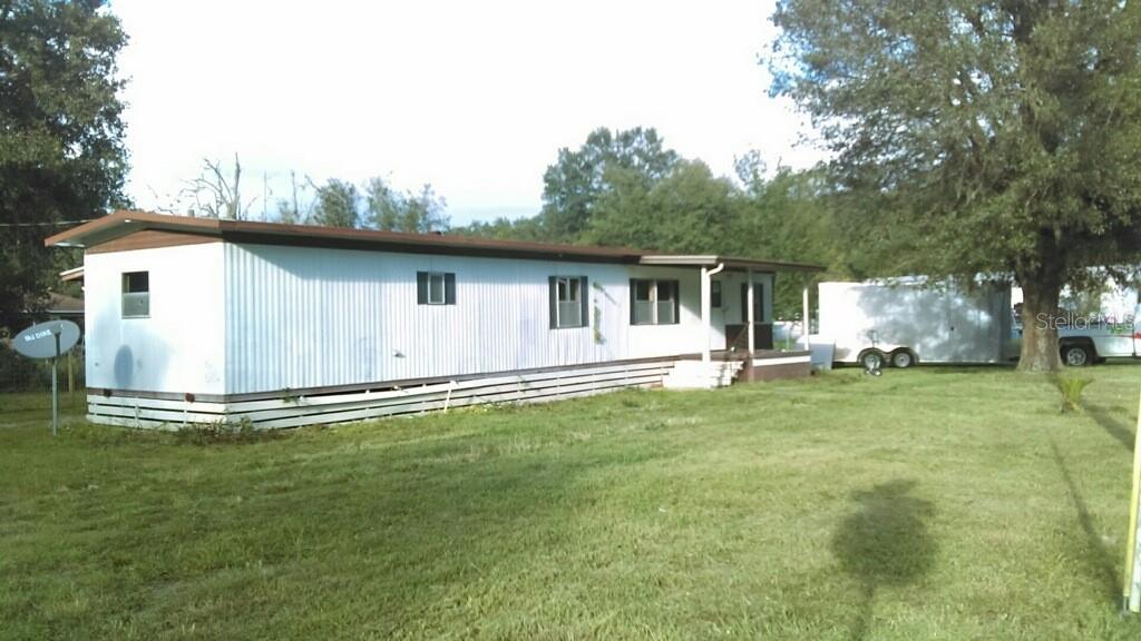 A single-story mobile home with white siding sits on a grassy lot with trees — 805 PETERS STREET, WILDWOOD, FL