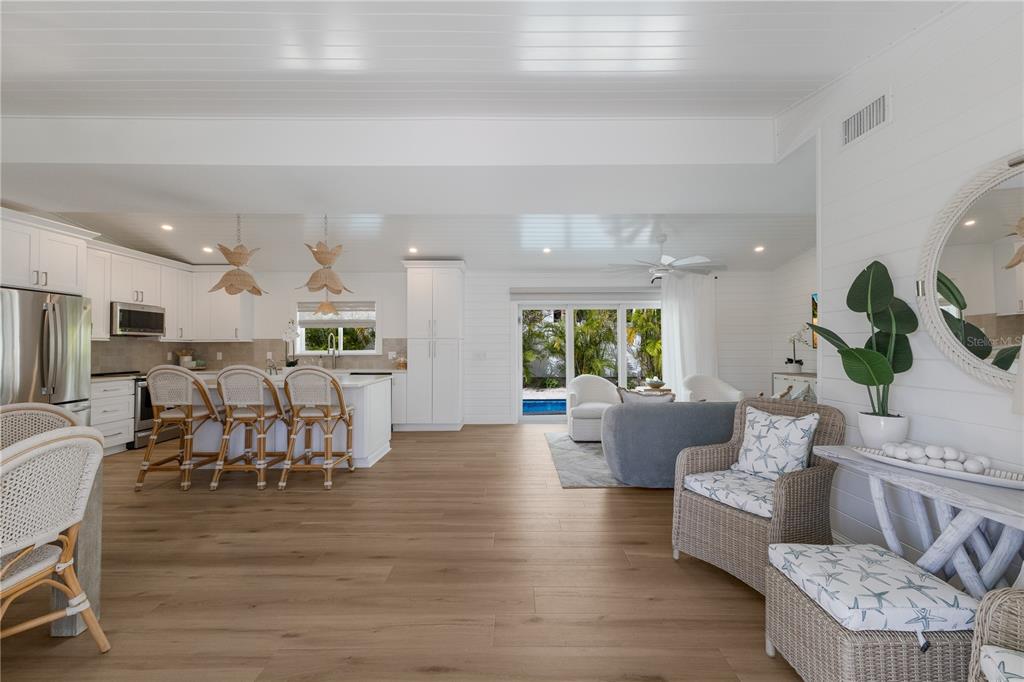 An open-concept kitchen and living area features white cabinetry, light wood flooring, and patio access — 401 N SHORE DRIVE, ANNA MARIA, FL