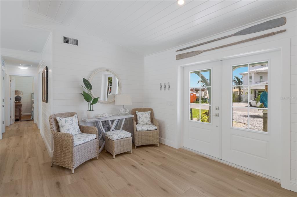 A bright entryway features white shiplap walls, light wood floors, wicker chairs, and double doors — 401 N SHORE DRIVE, ANNA MARIA, FL