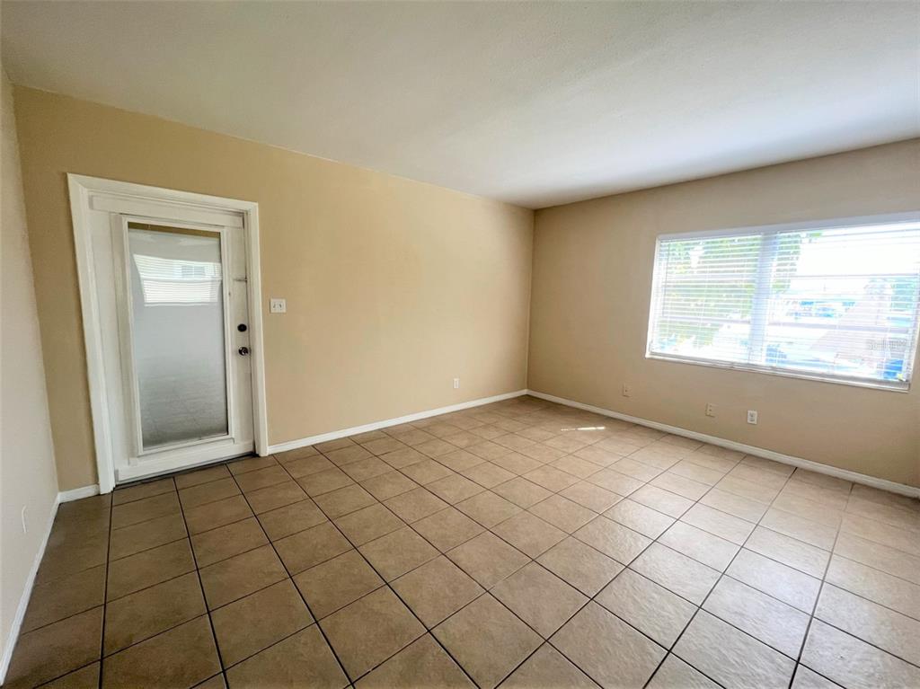 An empty room features beige walls, large square floor tiles, a glass door, and windows — 12175 3RD STREET E UNIT 2, TREASURE ISLAND, FL