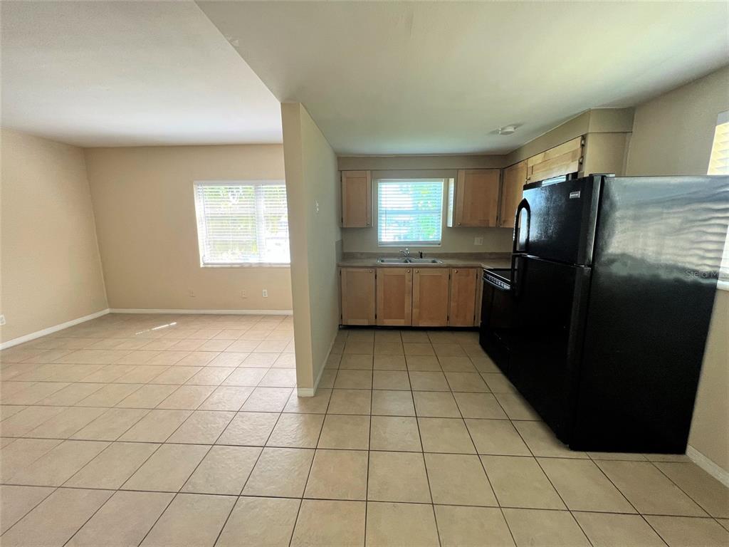 A kitchen with light wood cabinets and a black refrigerator opens to a tiled room — 12175 3RD STREET E UNIT 2, TREASURE ISLAND, FL