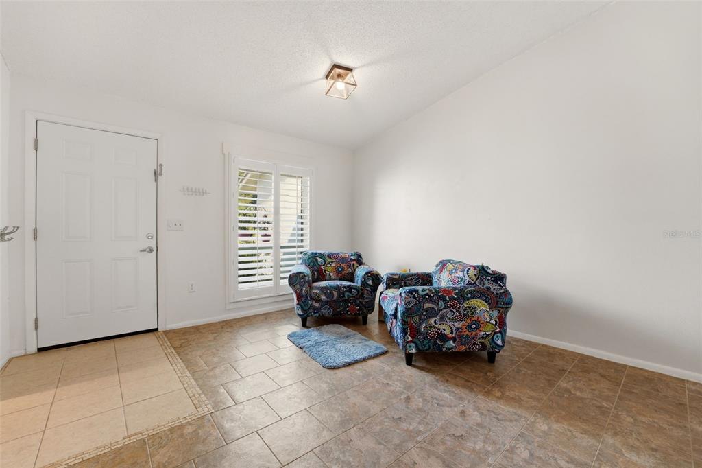 A room with tile flooring, white walls, a front door, and two patterned armchairs — 6132 29TH AVENUE W UNIT 6132, BRADENTON, FL