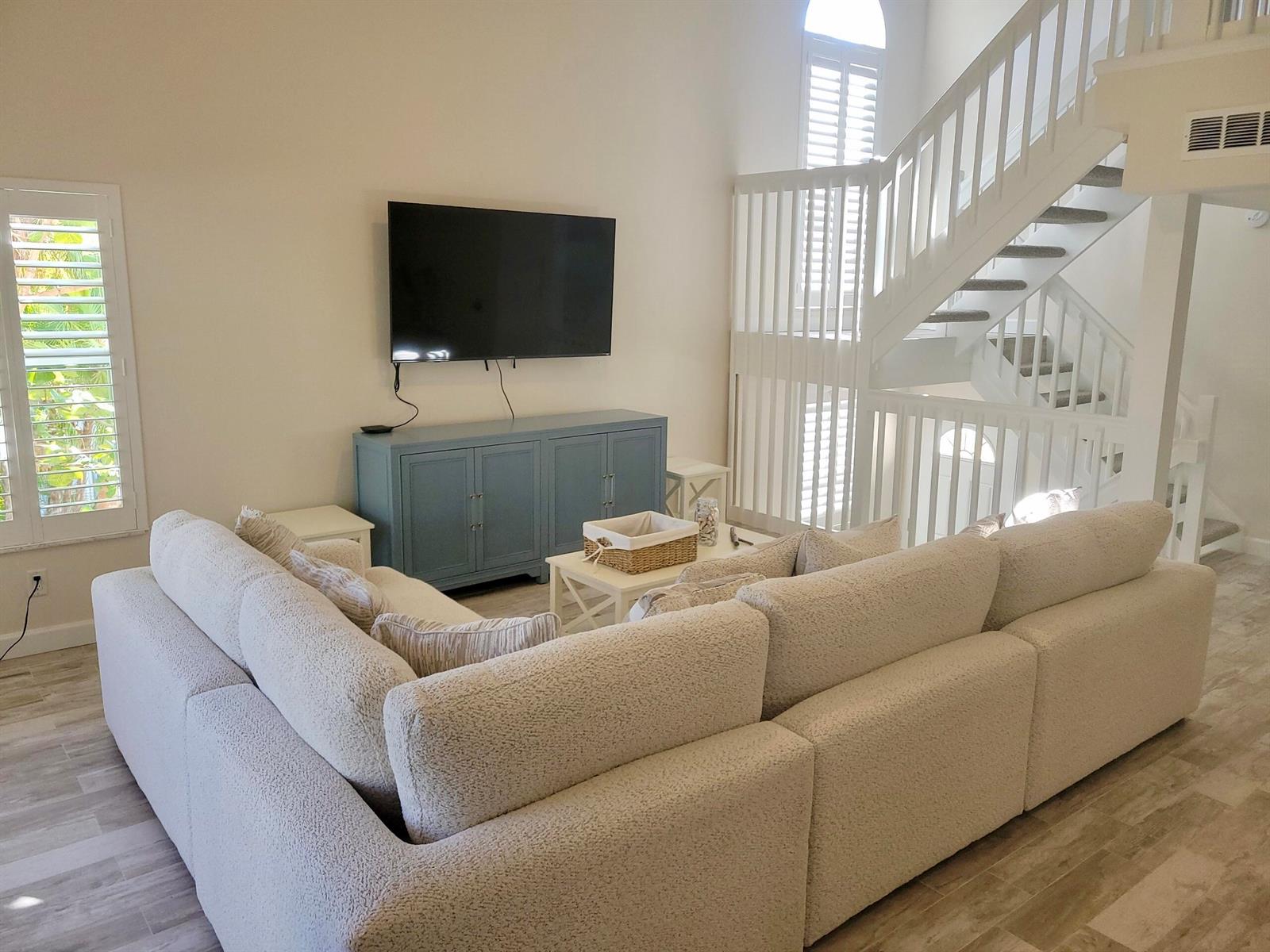 A living room features a large sectional sofa, a blue media console, and a staircase — 3108 Fairway Drive N, Jupiter FL 33477, JUPITER, FL