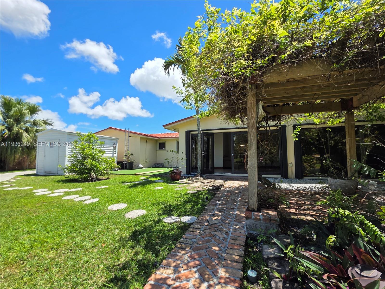 A brick walkway leads to a patio with a wooden pergola and a grassy backyard — 14545 SW 75th St, Miami FL 33183, MIAMI, FL
