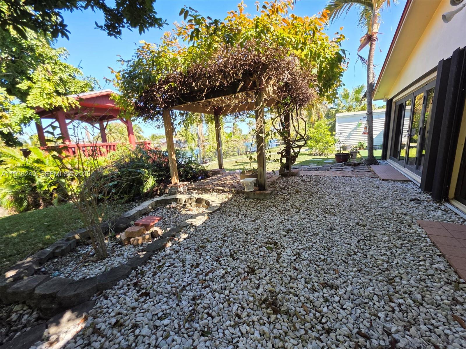 A backyard features a gravel patio, a wooden pergola with climbing vines, and a gazebo — 14545 SW 75th St, Miami FL 33183, MIAMI, FL