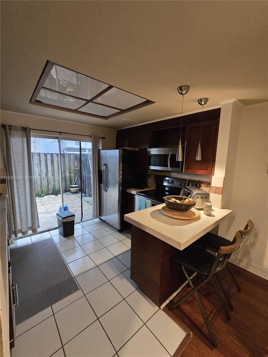 A kitchen features dark wood cabinets, stainless steel appliances, a breakfast bar, and sliding glass doors — 7010 NW 173rd Dr # 1901, Hialeah FL 33015, HIALEAH, FL