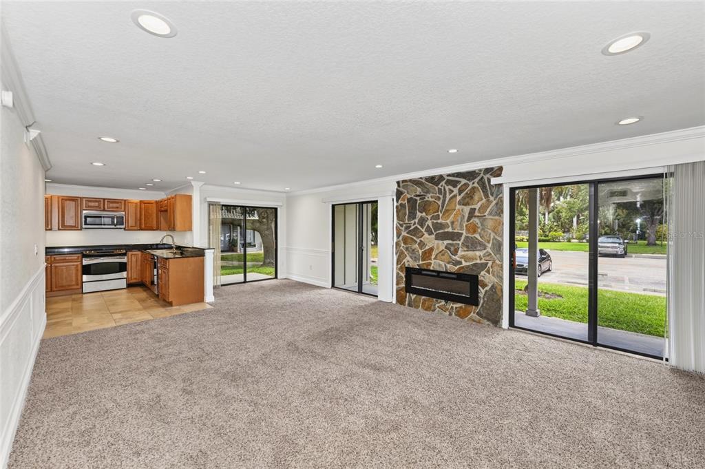 A living room with carpet, a stone fireplace, and an adjacent kitchen with wooden cabinets — 2220 BAHIA VISTA STREET UNIT G4, SARASOTA, FL