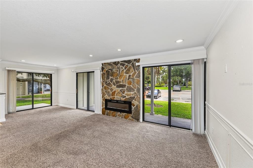 A living room features beige carpeting, a stone fireplace, and multiple sliding glass patio doors — 2220 BAHIA VISTA STREET UNIT G4, SARASOTA, FL