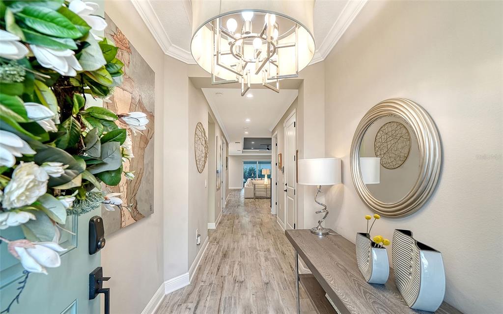 A bright entryway features a chandelier, a console table with a mirror, and wood-look flooring — 12635 NIGHT VIEW DRIVE, SARASOTA, FL